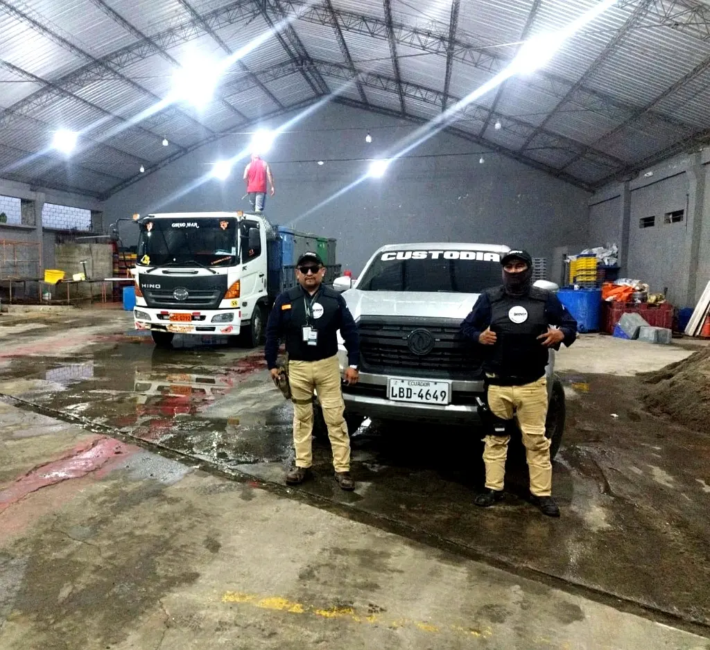 Custodios armados de GEOVIP junto a una camioneta de custodia y un camión de carga